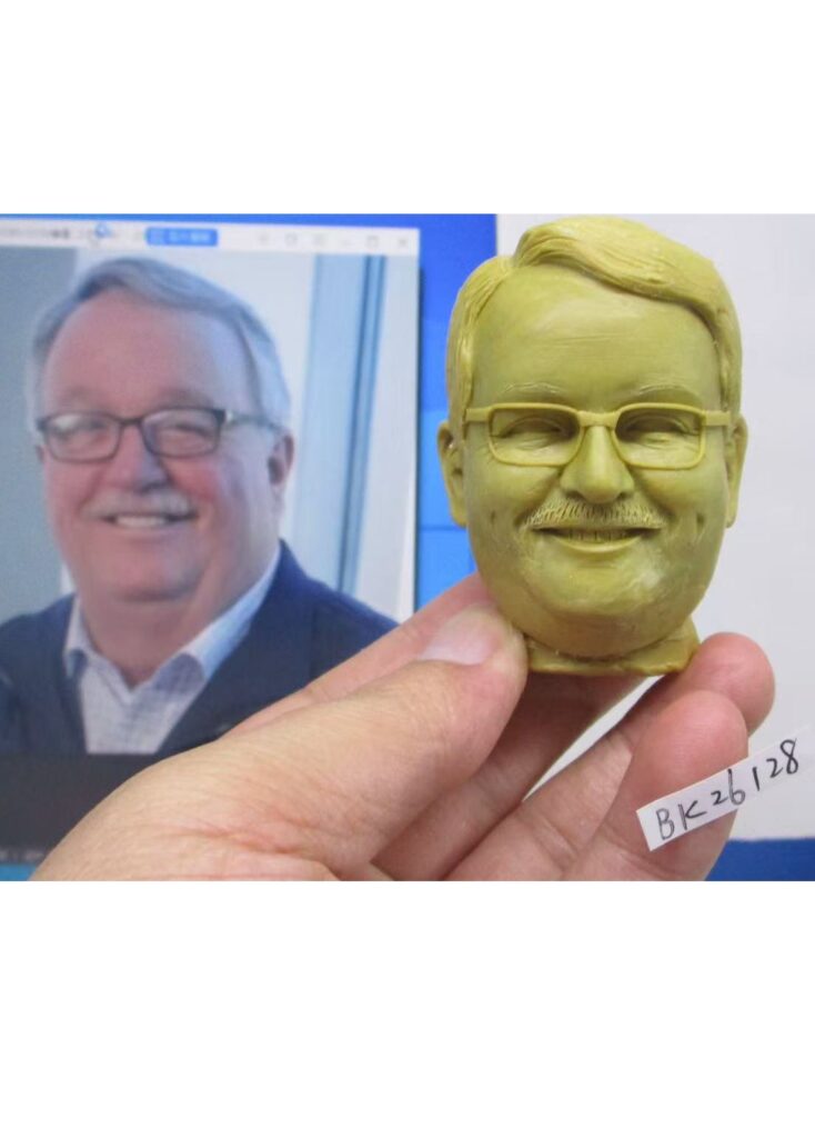 Hand-sculpted clay head prototype of Bob Jameson beside his reference photo for a custom retirement bobblehead.